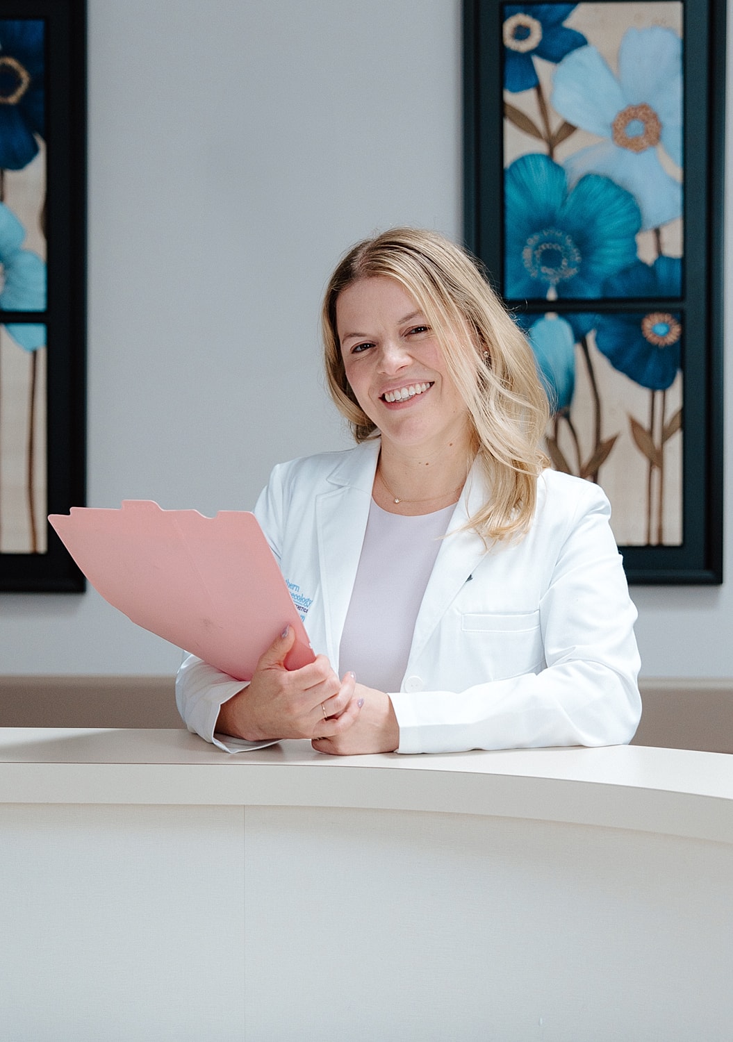Woman in white coat holding pink folder.